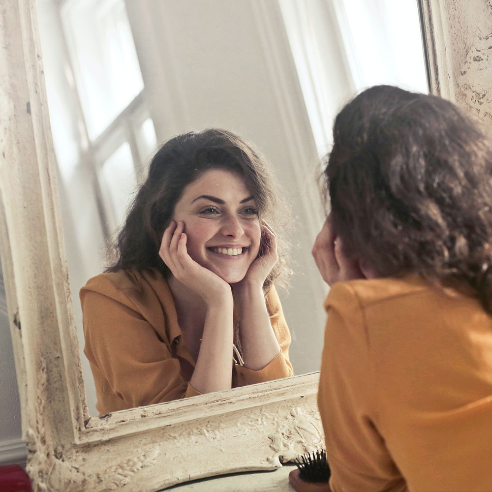 Önbizalommal teli nő mosolyog a tükörben.